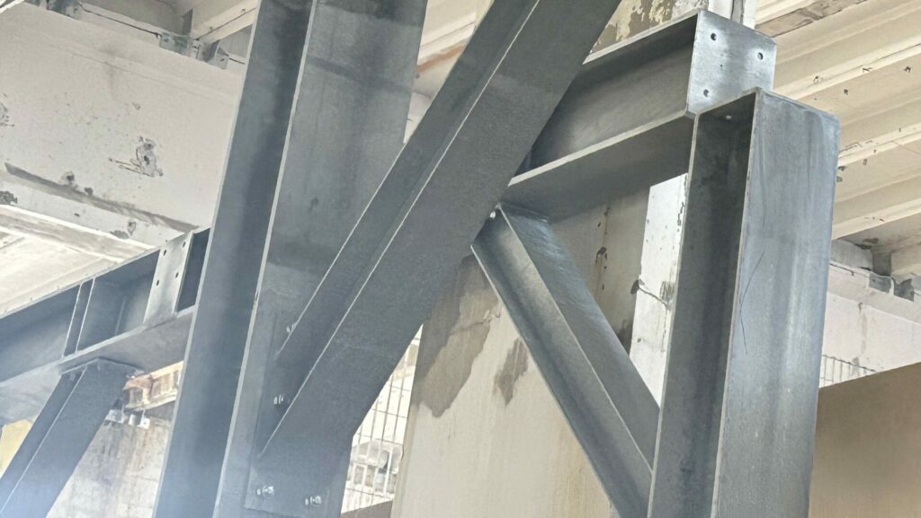Strutture in acciaio grigie che si intersecano davanti a un muro sullo sfondo