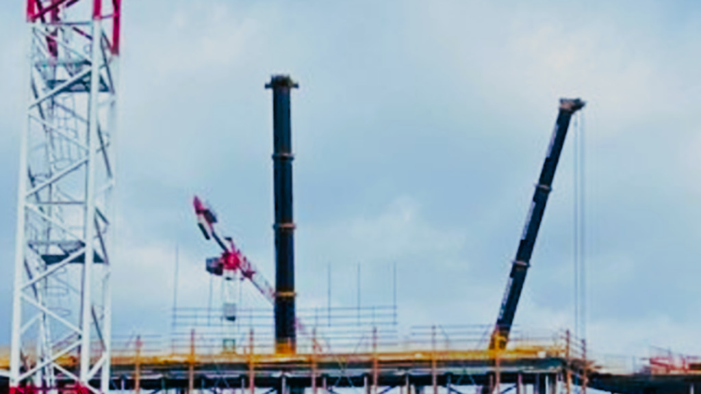 Immagine di un cantiere edile con gru a torre e gru mobili impegnate nella costruzione di una struttura multipiano in acciaio e cemento, simbolo dell’importanza della sicurezza e classificazione delle gru secondo la nuova norma UNI ISO 4301-5:2025.