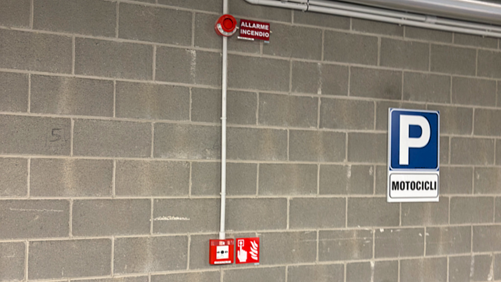 Segnaletica antincendio e cartello parcheggio motocicli su parete in cemento, installazione relativa alla Nuova UNI 11988 per sistemi di allarme vocale in un cantiere CED INGEGNERIA.